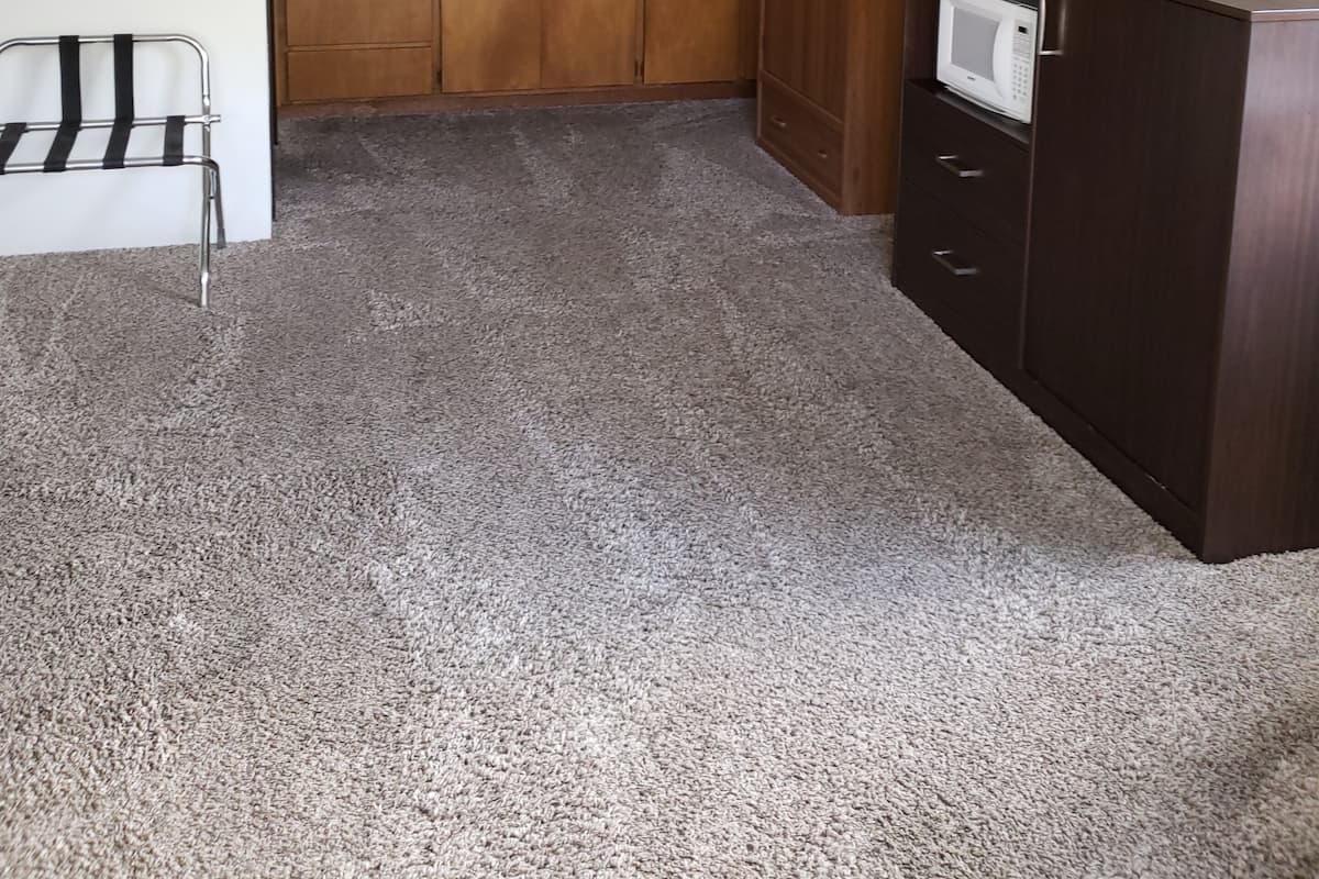 Cocina compacta con armarios de madera, microondas y una pequeña zona de estar con una silla de metal.