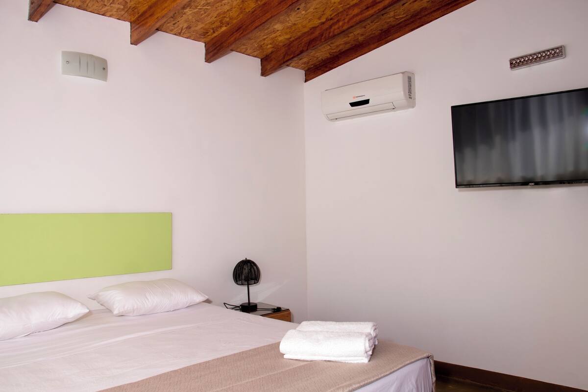 A bedroom with a bed, a bedside table, a wall-mounted TV, and an air conditioning unit.