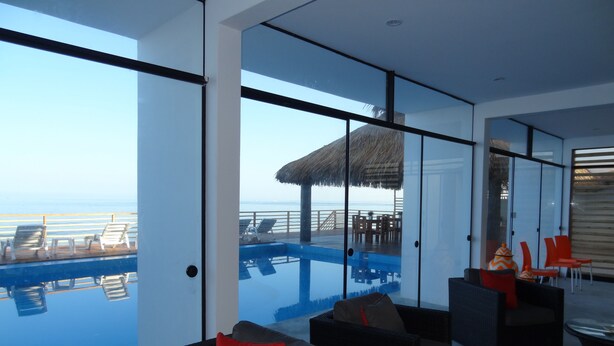 A modern interior with a glass infinity pool, a thatched-roof structure, and outdoor seating by the pool. - Akas Hotel Apartamentos (Canoas de Punta Sal)