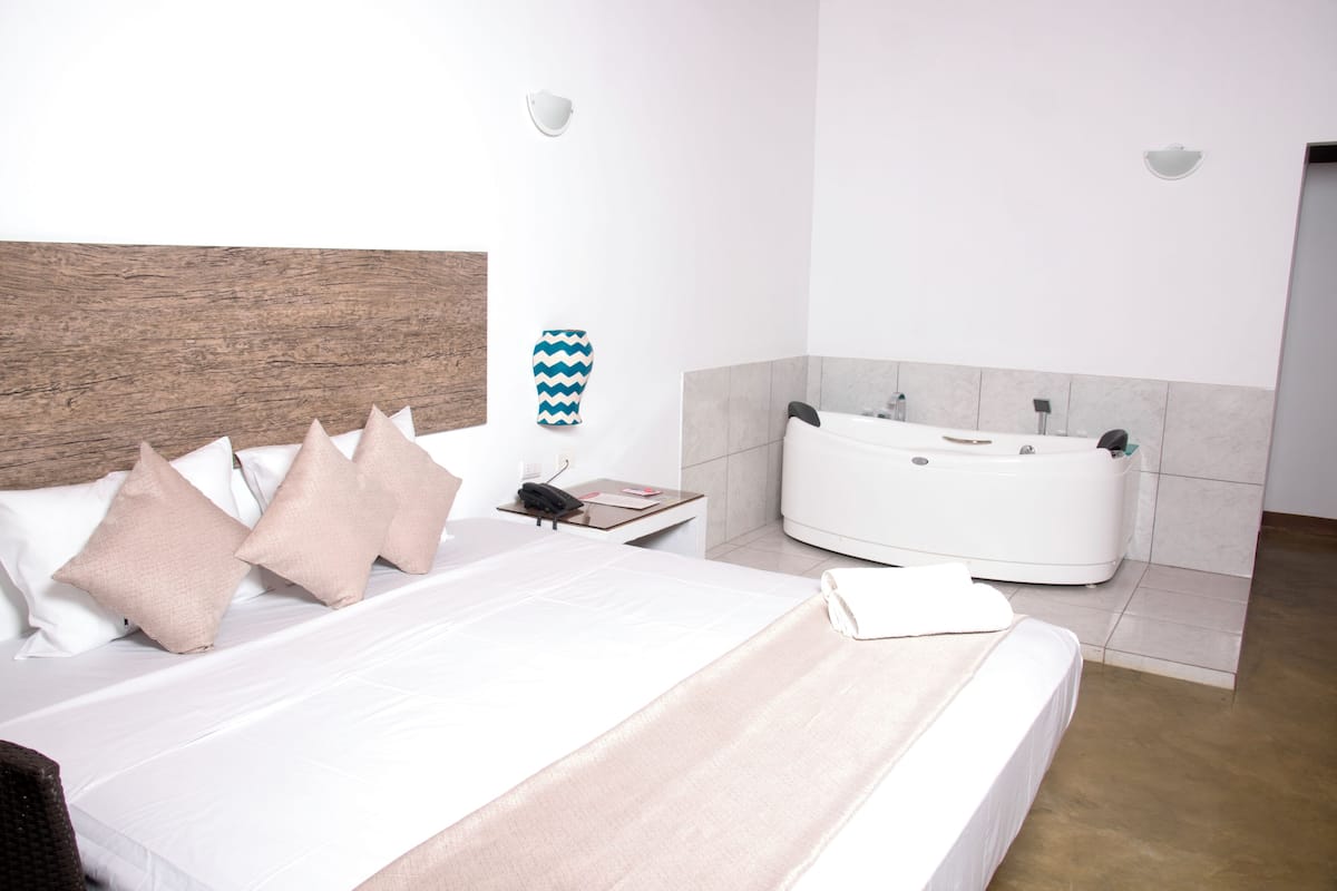 A hotel room with a bed, a bedside table, a phone, a vase, and a bathtub.