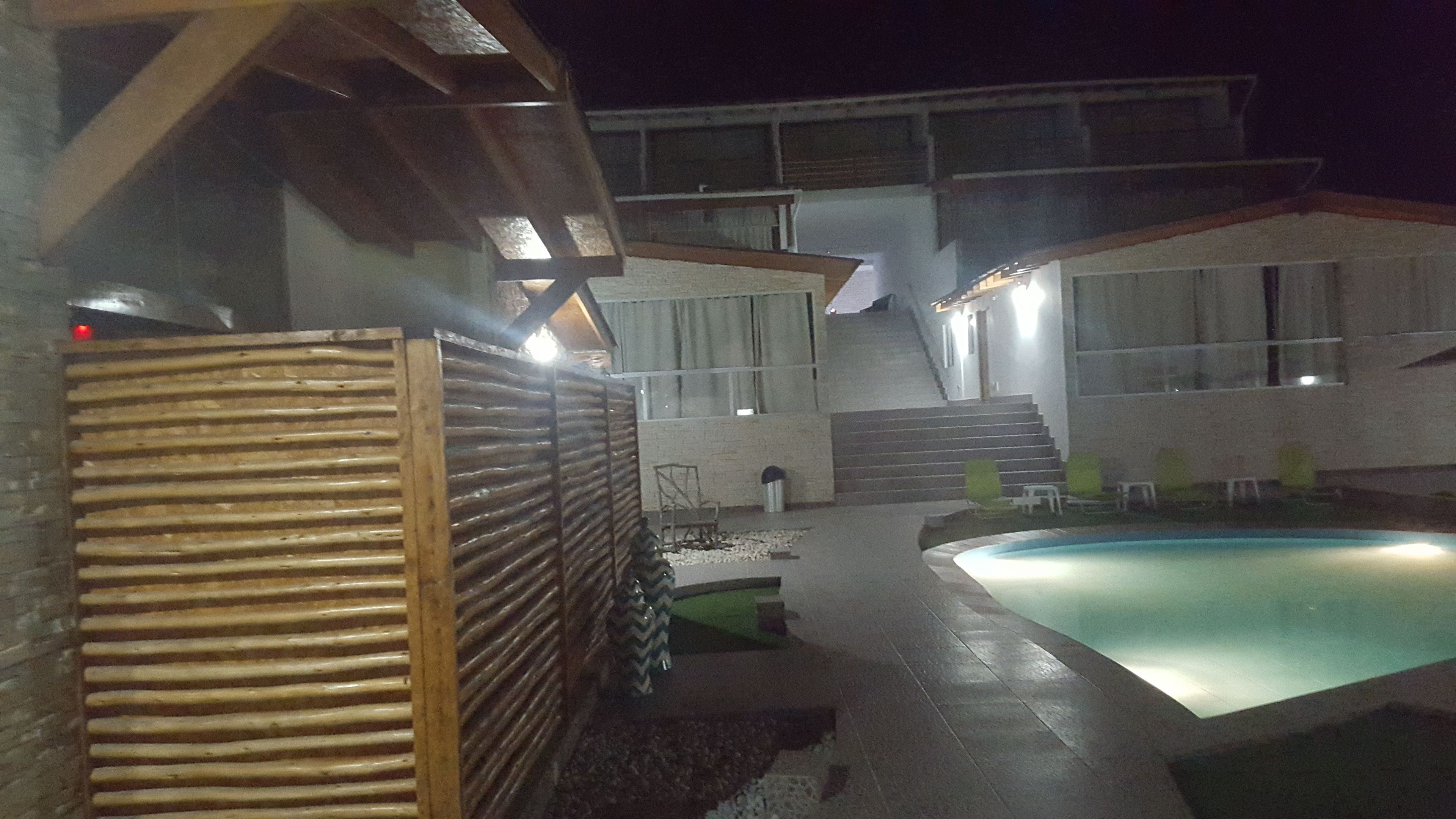 Un área de piscina con cubierta de madera, una zona de estar techada y una escalera que lleva a un segundo nivel.