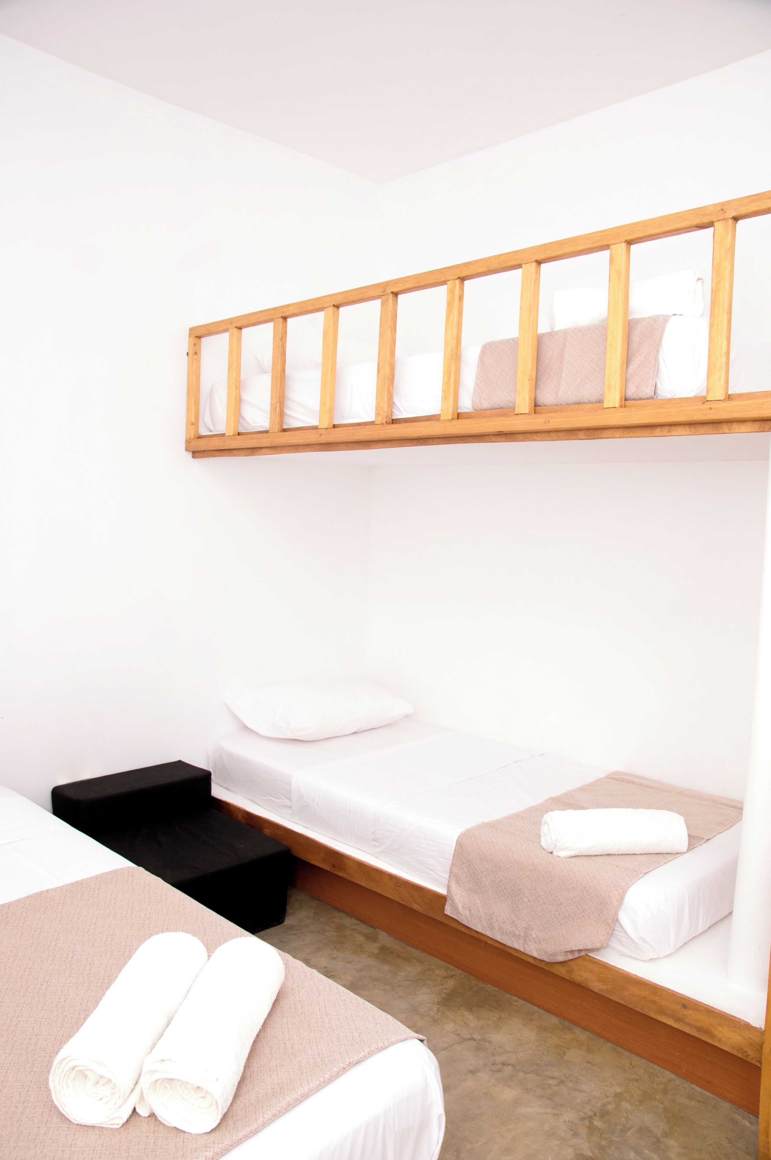 A room with two beds, a wooden bunk bed above, and a black bench.