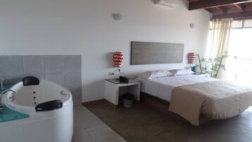 Habitación de hotel con bañera, cama, mesita de noche, calefactor en la pared y ventana con cortinas.