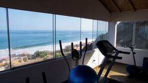 A gym with exercise equipment and a large window overlooking the ocean. - Akas Hotel Apartamentos (Canoas de Punta Sal)