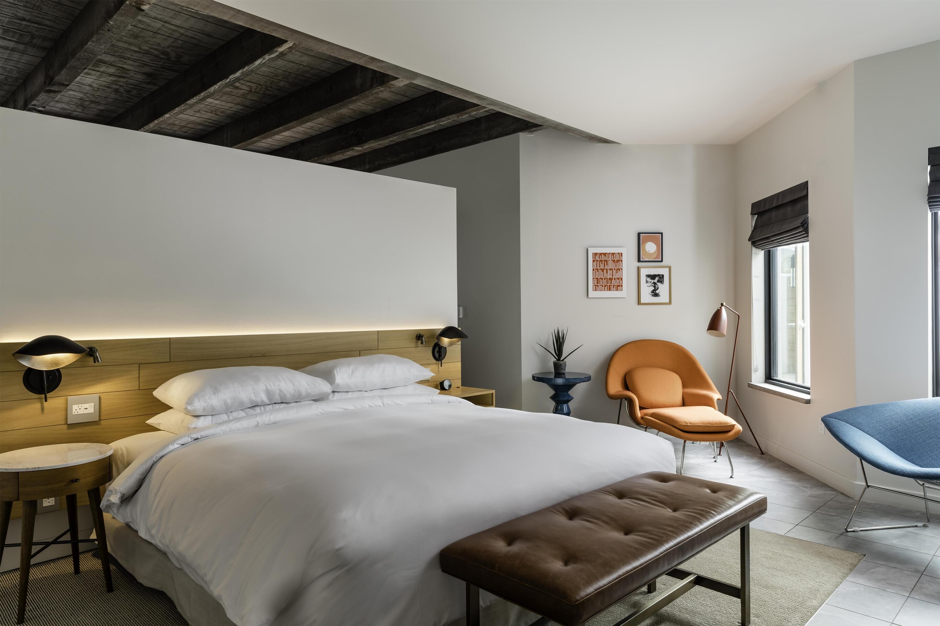 Une chambre d’hôtel moderne avec un grand lit, une banquette, une chaise, une petite table et une fenêtre donnant sur un beau paysage.