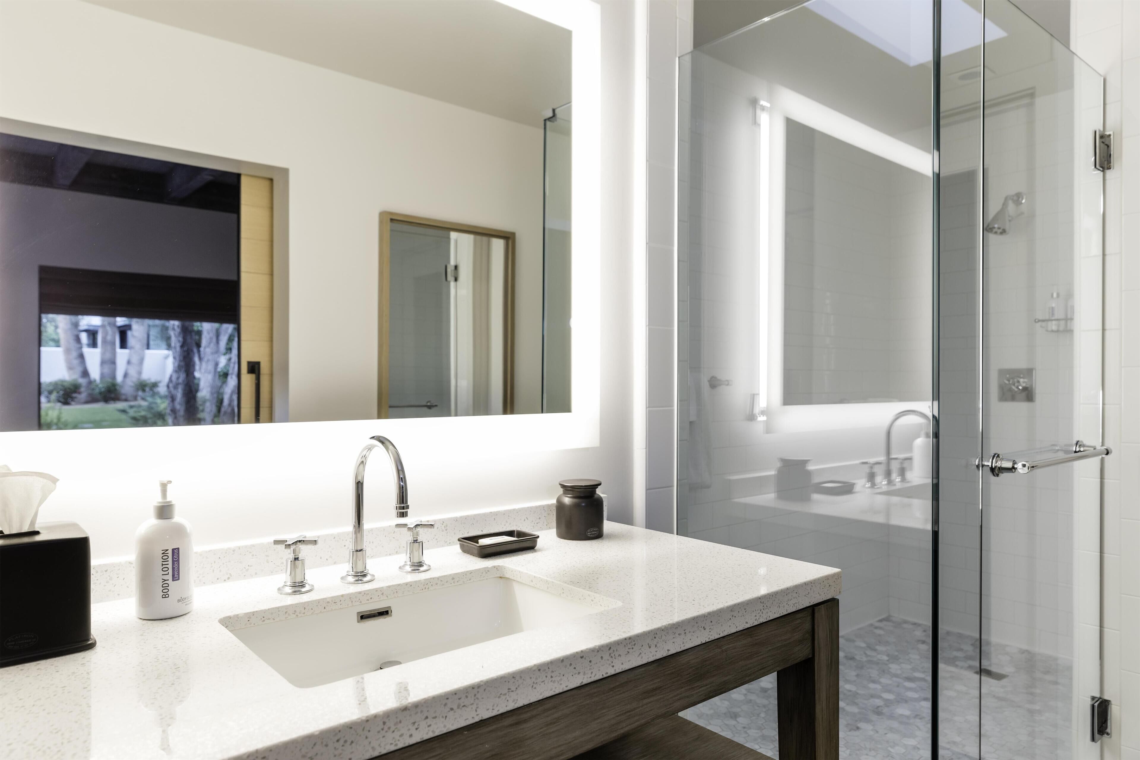 A modern bathroom with a large mirror, a white sink, and a glass shower enclosure.