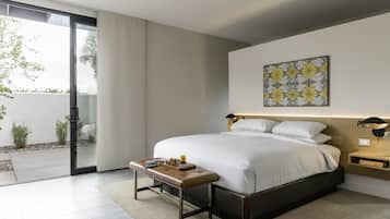 Ein modernes Schlafzimmer mit einem großen Bett, einer Bank, einem Nachttisch und Blick durch eine Schiebetür auf einen Außenbereich.