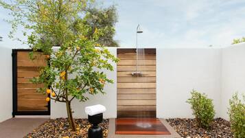 A modern outdoor shower area with a wooden wall, a tree with oranges, and a black sculpture.