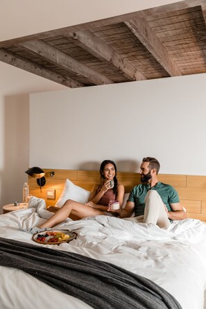 A couple sitting on a bed with a wooden headboard, a bedside table with a lamp, and a fruit plate.