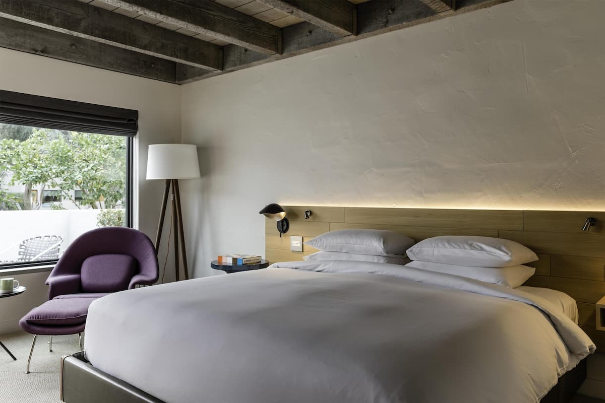 Une chambre d’hôtel moderne, dotée d’un grand lit, d’une chaise, d’une lampe et offrant une vue sur l’extérieur.