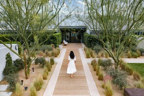 A woman walking on a wooden pathway towards a modern building with glass doors.