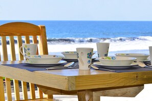 A wooden table set with white plates, bowls, and a pitcher, overlooking the ocean. - Playa Plana Hotel (Chiquimulilla)