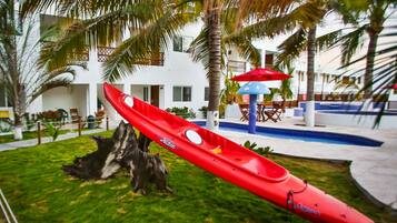 Kayaks and poolside seating await in a serene outdoor area surrounded by palm trees and a charming building.