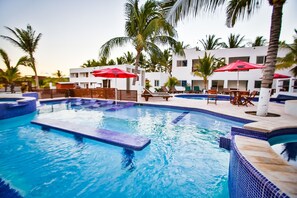 A swimming pool with lounge chairs and umbrellas, surrounded by palm trees and a white building. - Playa Plana Hotel (Chiquimulilla)