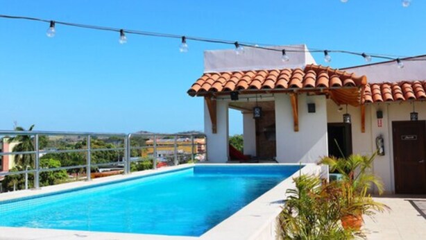 A swimming pool with a tiled roof structure adjacent to it. - Hotel Presidente (Las Tablas)