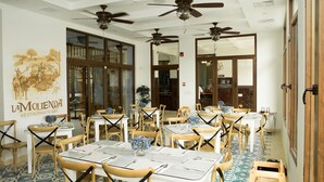 A restaurant with tables set for dining, wooden chairs, ceiling fans, and a mural on the wall. - Hotel Presidente (Las Tablas)