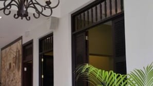 A hallway with a chandelier, a wooden door, and a window with shutters. - Hotel Presidente (Las Tablas)