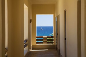 A hallway leading to a balcony with a view of the sea and a sailboat.