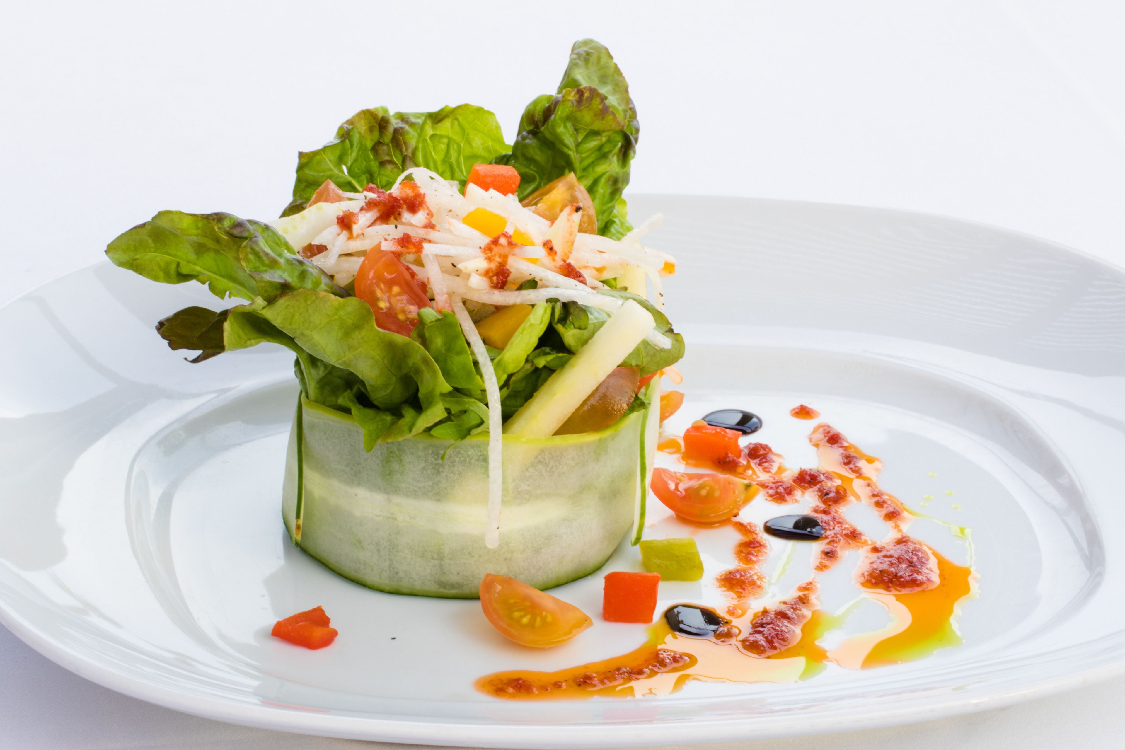 Ein weißer Teller mit einem Salat vor weißem Hintergrund.