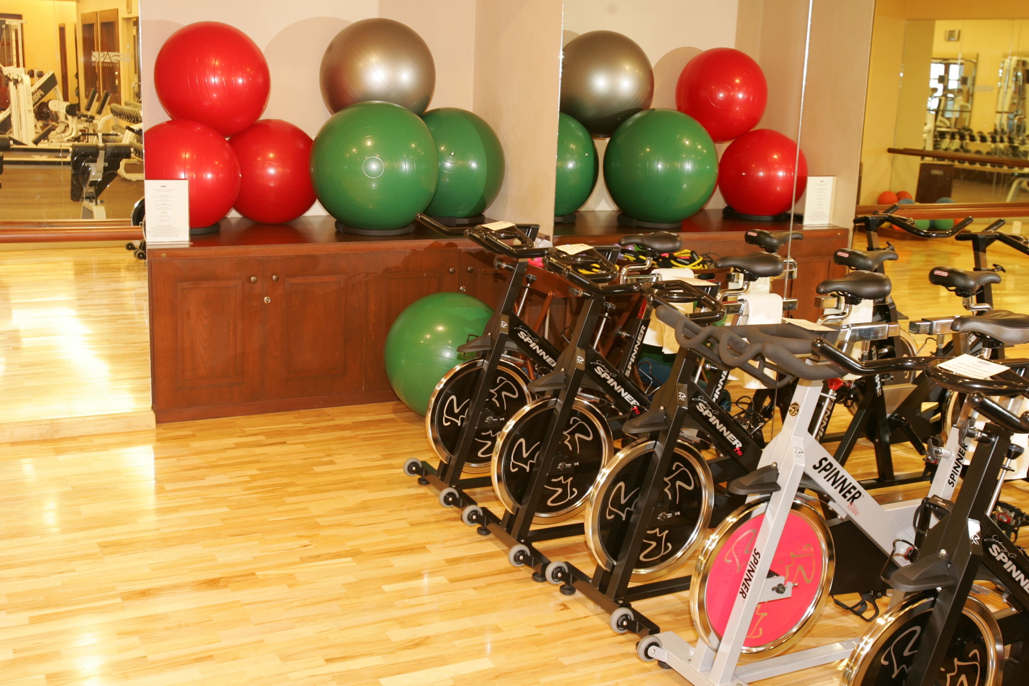 A gym with stationary bikes, exercise balls, and a wooden floor.