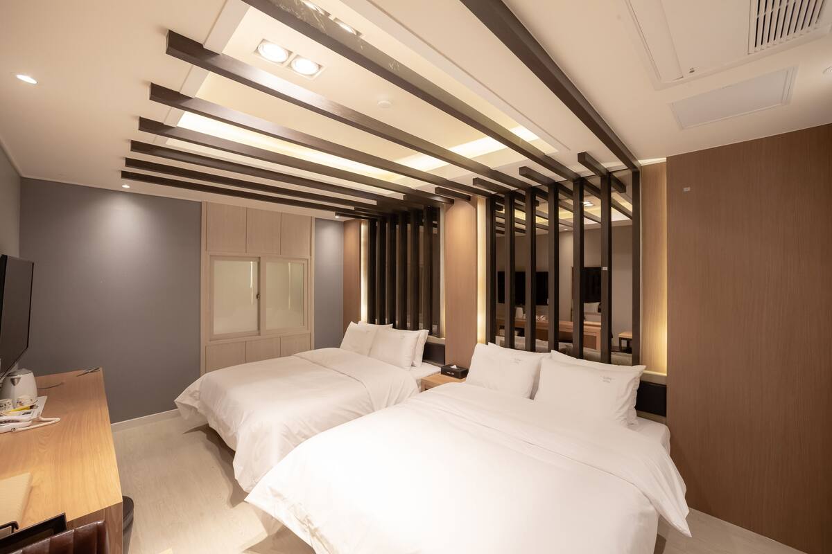 A hotel room with two beds, a desk, and a TV.