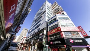 Un edificio de varios pisos con diversos establecimientos comerciales en la planta baja, incluyendo una tienda 'SQUARE' visible.