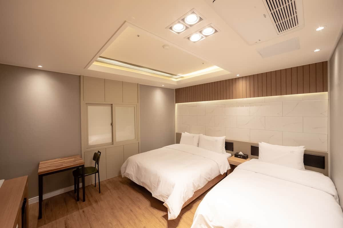 A modern hotel room with two beds, a desk, and a chair.