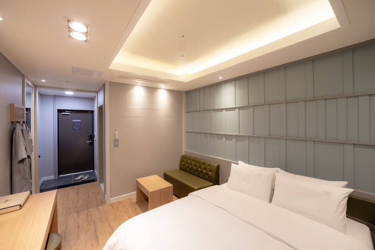 A modern hotel room with a large bed, a small seating area, a desk, and a wardrobe.