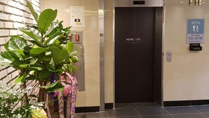 Un vestíbulo de hotel con una mesa de recepción, un lector de tarjetas llave instalado en la pared y un ascensor que indica “11F”.