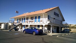 A two-story motel with a red-tiled roof, a staircase leading to the upper floor, and a parking lot with a blue car. - Backcountry Inn Motel (Boulevard)