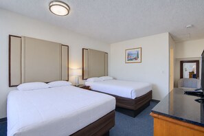 Une chambre d’hôtel avec deux lits, une table de chevet avec une lampe, un tableau au mur et une salle de bain visible à travers une porte ouverte.