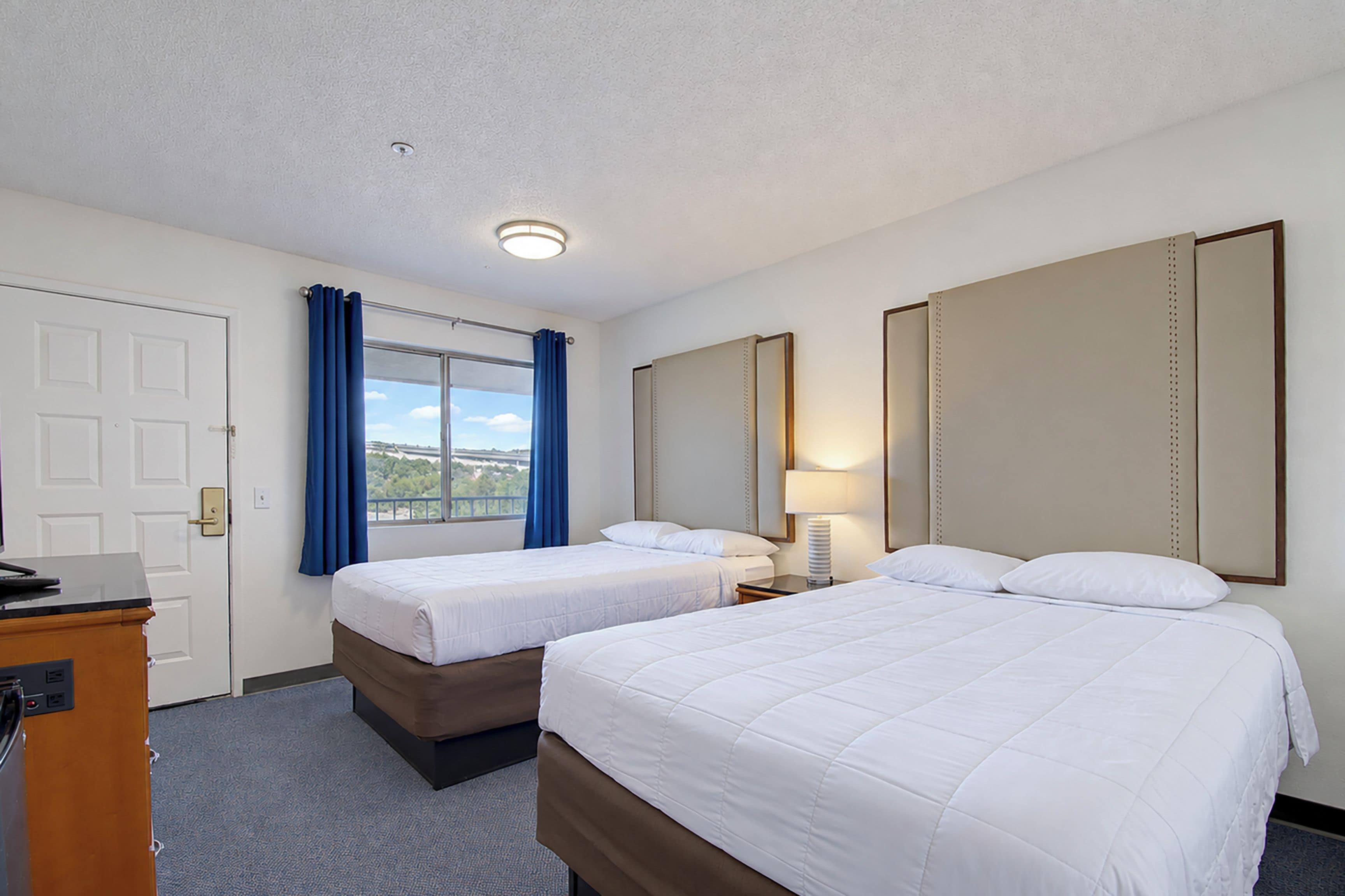 Una habitación de hotel con dos camas, un escritorio, una lámpara y un espejo grande.