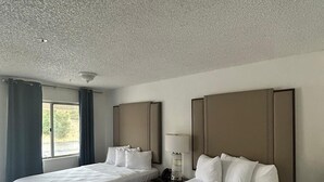 A hotel room with two beds, a bedside table with a lamp, and a window with curtains. - Backcountry Inn Motel (Boulevard)