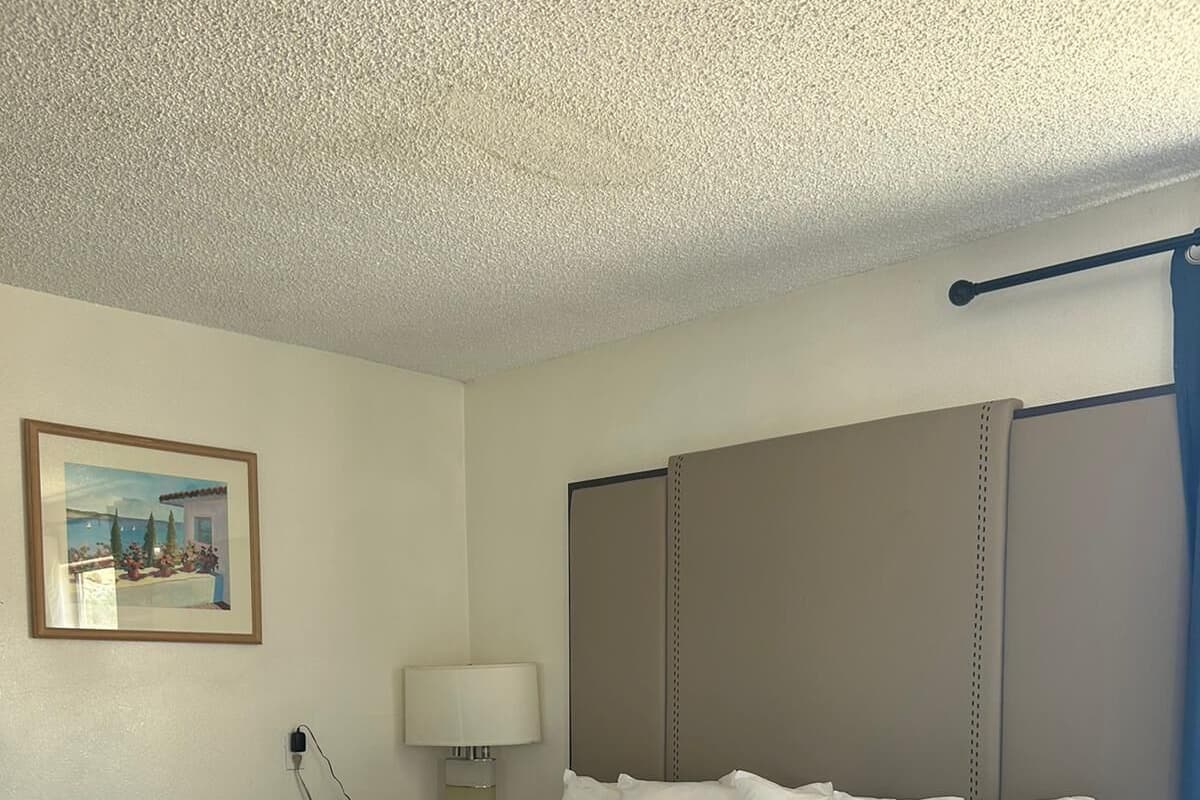 A hotel room with a large bed, a nightstand with a lamp, a painting on the wall, and a window with curtains.
