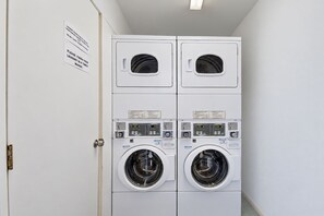 A laundry room with two stacked washing machines and a dryer, a door with a sign, and a light fixture on the ceiling. - Back Country Inn Boulevard, CA (Boulevard)