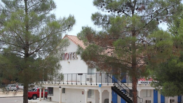 A motel with a white facade, a red truck parked in front, and a staircase leading to the entrance. - Backcountry Inn Motel (Boulevard)