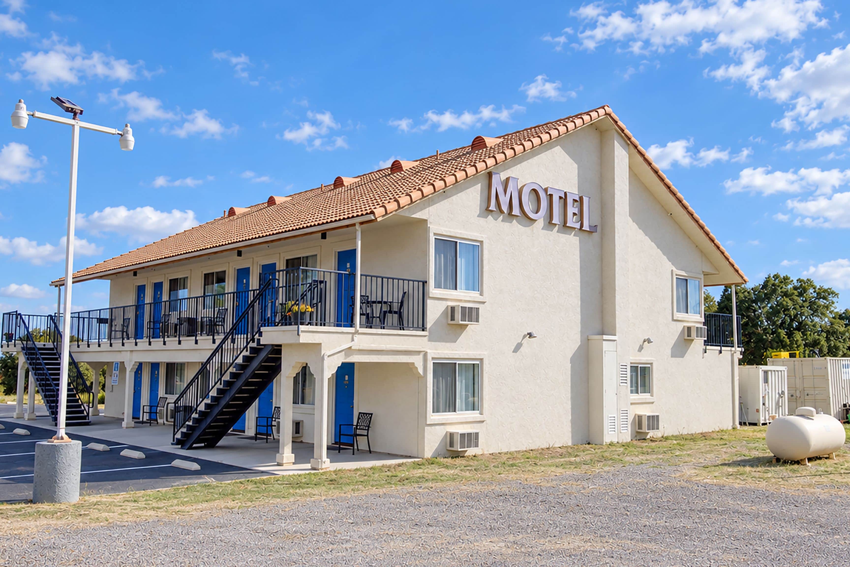 A two-story motel with a tiled roof, a balcony on the upper floor, and a staircase leading to the entrance.