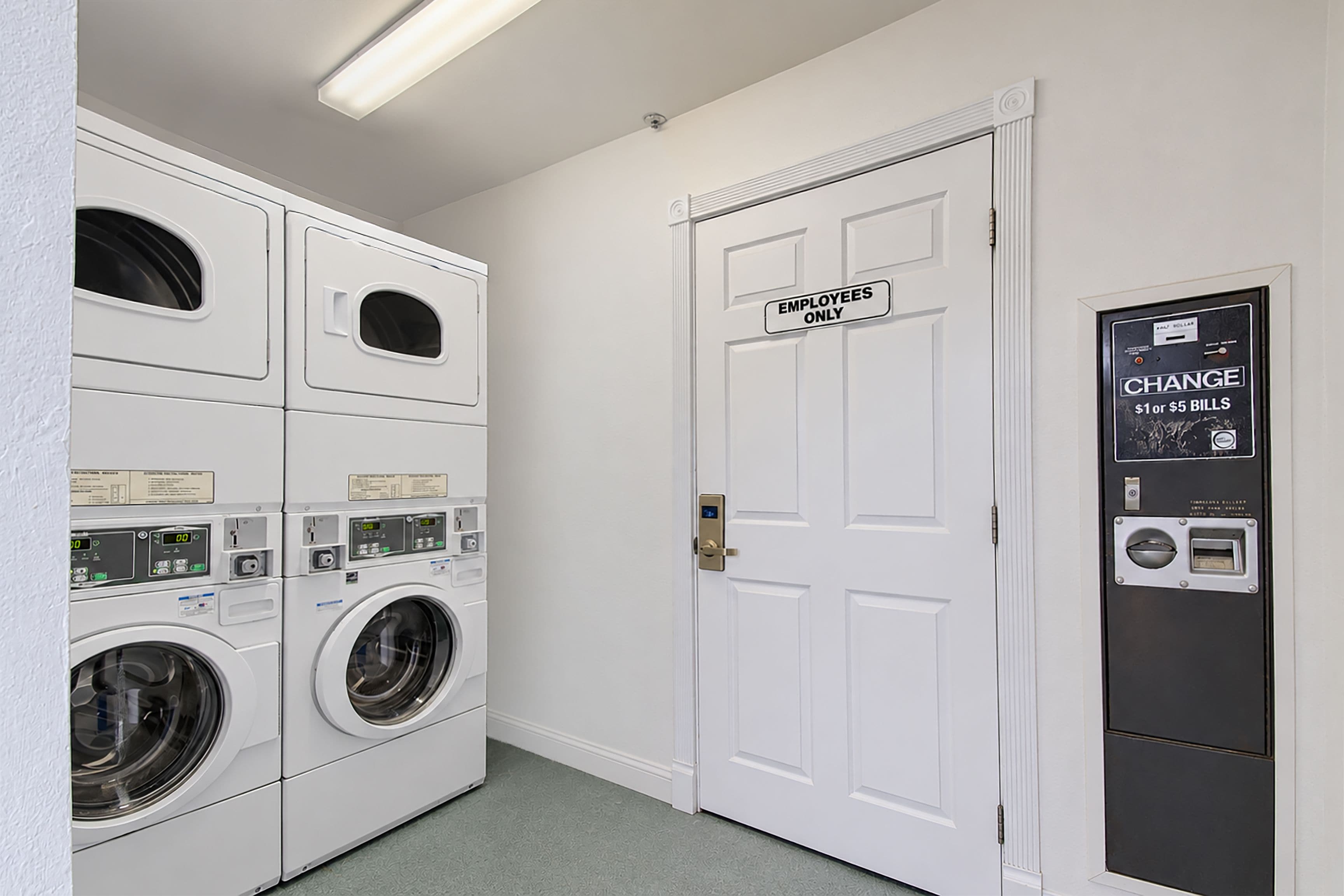 A laundry room with stacked washers and dryers, a door marked 'Employees Only,' and a change machine.