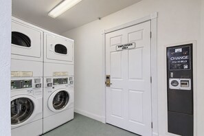 A laundry room with stacked washers and dryers, a door marked 'Employees Only,' and a change machine. - Back Country Inn Boulevard, CA (Boulevard)
