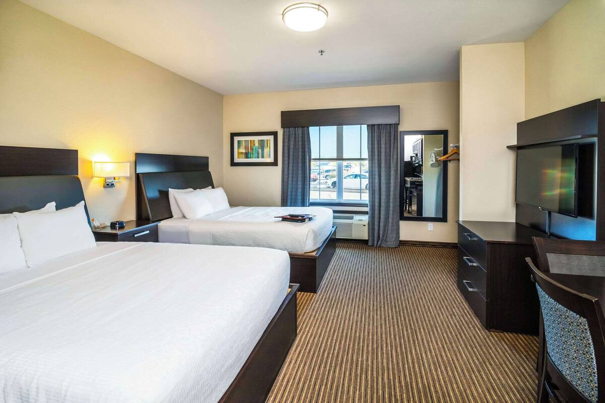 Une chambre d’hôtel avec deux lits, un téléviseur à écran plat, un bureau et une fenêtre avec des rideaux.