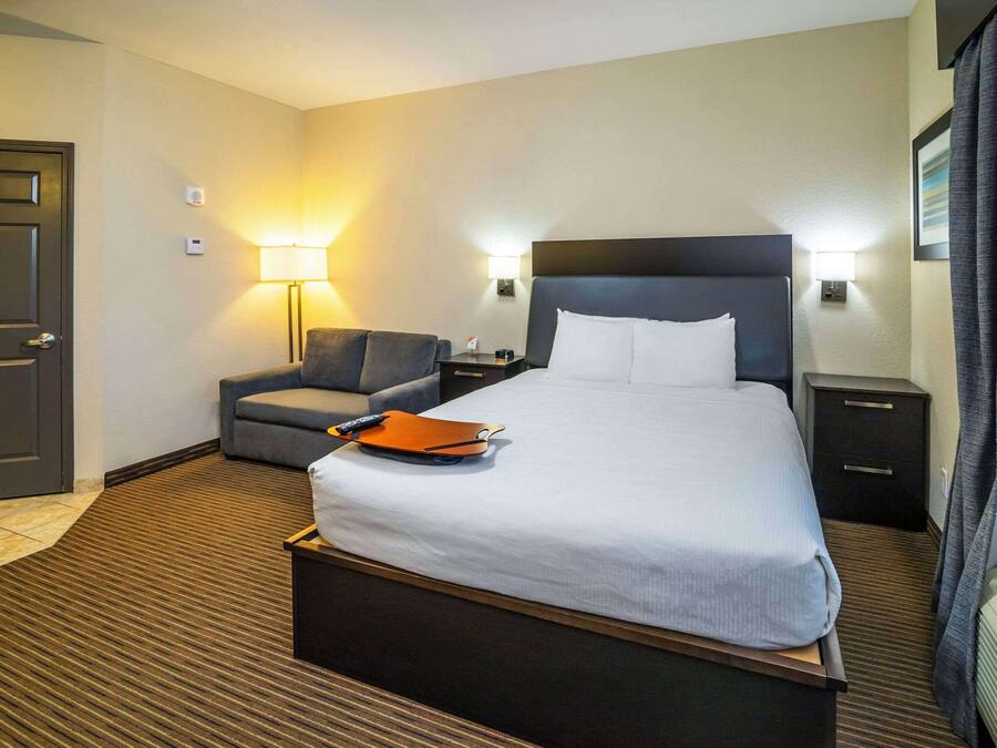 A hotel room with a large bed, a desk, a chair, and a lamp.
