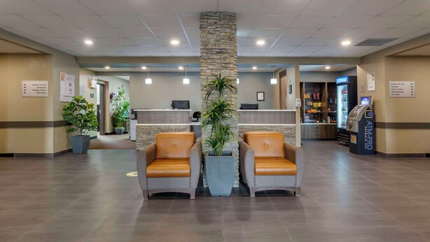 A hotel lobby with a reception desk, two leather chairs, potted plants, and an ATM machine.