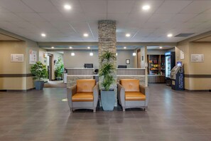 A hotel lobby with a reception desk, two leather chairs, potted plants, and an ATM machine. - Quality Inn & Suites Moose Jaw (Moose Jaw)