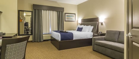 Habitación de hotel con cama, escritorio, silla, sofá, televisor y ventana con cortinas.