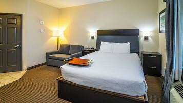 A hotel room with a large bed, a desk, a chair, a lamp, and a door.