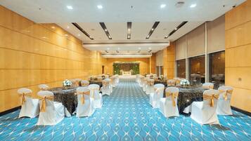 A conference room with a blue patterned carpet, white chairs with gold sashes, and a floral backdrop at the front.