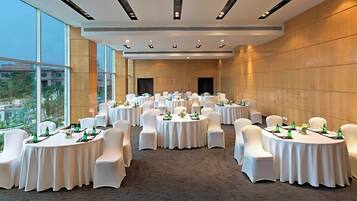 A conference room with multiple round tables, white chairs, and green bottles on each table.