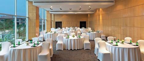 A conference room with multiple round tables, white chairs, and green bottles on each table.