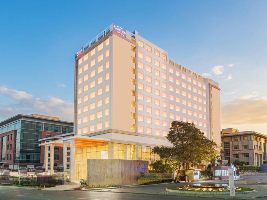 Un hotel de varios pisos con un letrero llamativo, una entrada bien iluminada y un área ajardinada con una fuente.