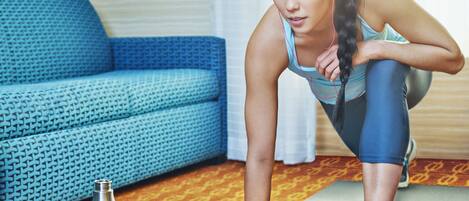 A person in workout attire on a yoga mat in a room with a patterned sofa and a metallic water bottle on the floor.